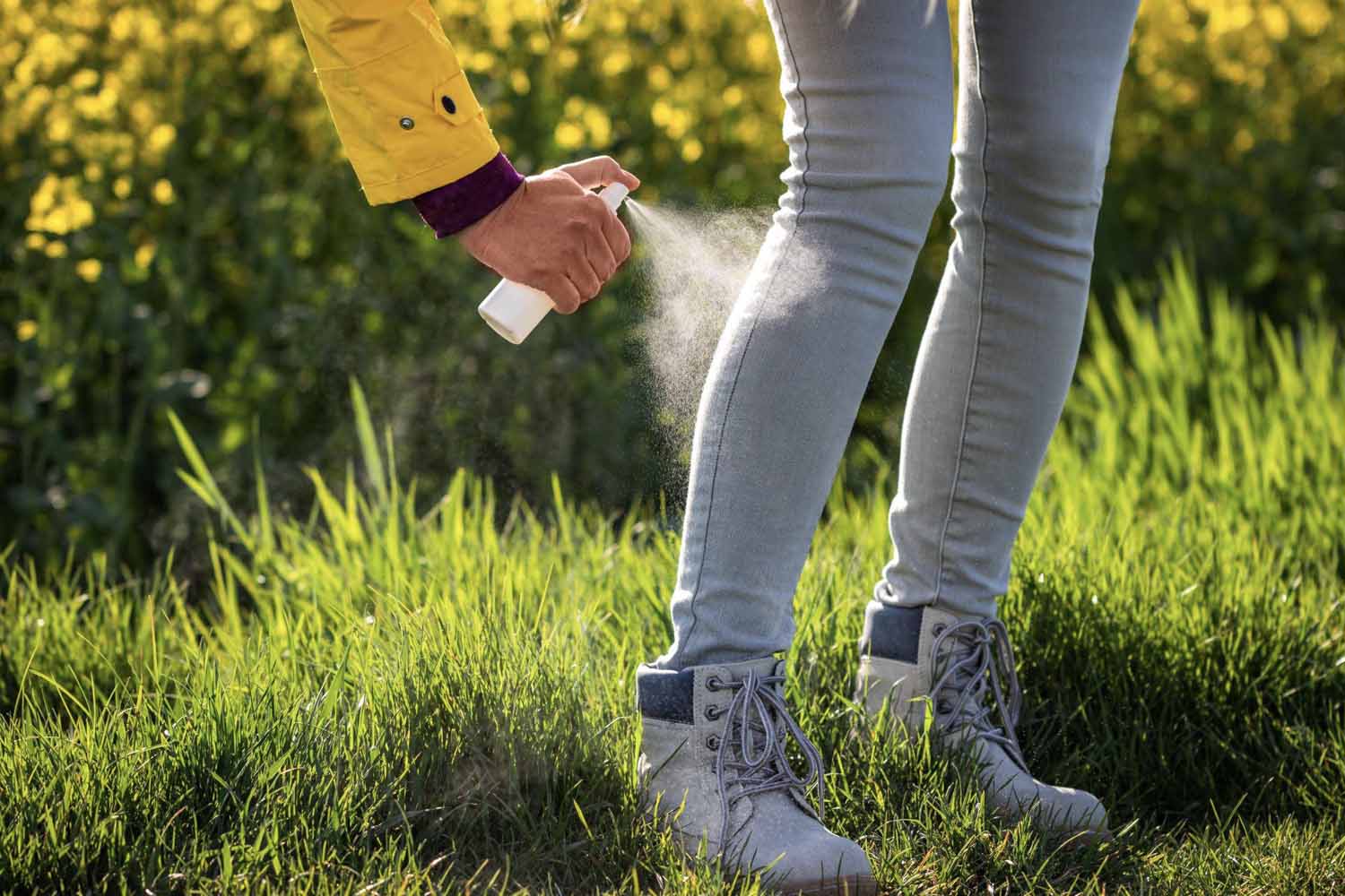 Person spraying insect repellent on pants and boots to protect against ticks and mosquitoes.