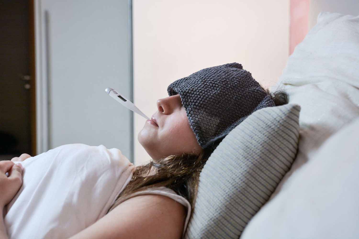 Woman laying down with a cold cloth on her forehead and a thermometer in her mouth