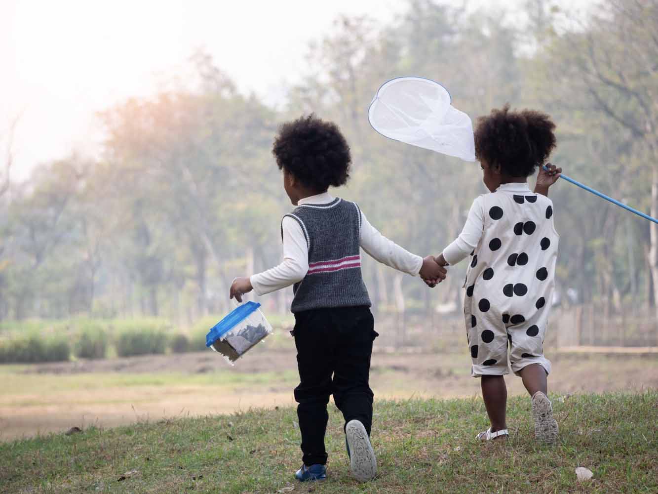 little boy carrying a bug collection box holding hands with little girl carrying a net to catch insects