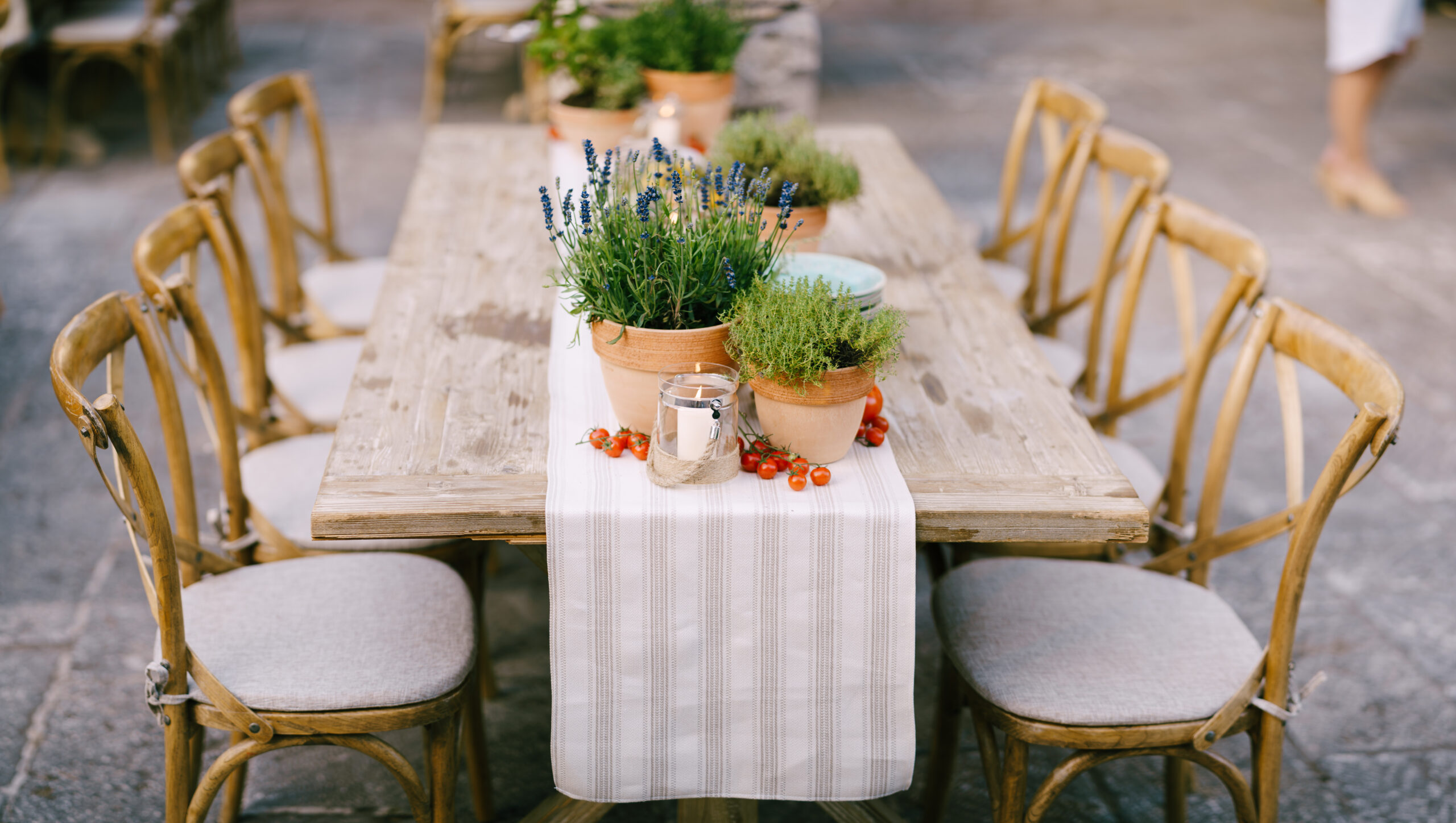 Outdoor dining table with pots of lavender and citronella candles in the center on a linen table runner