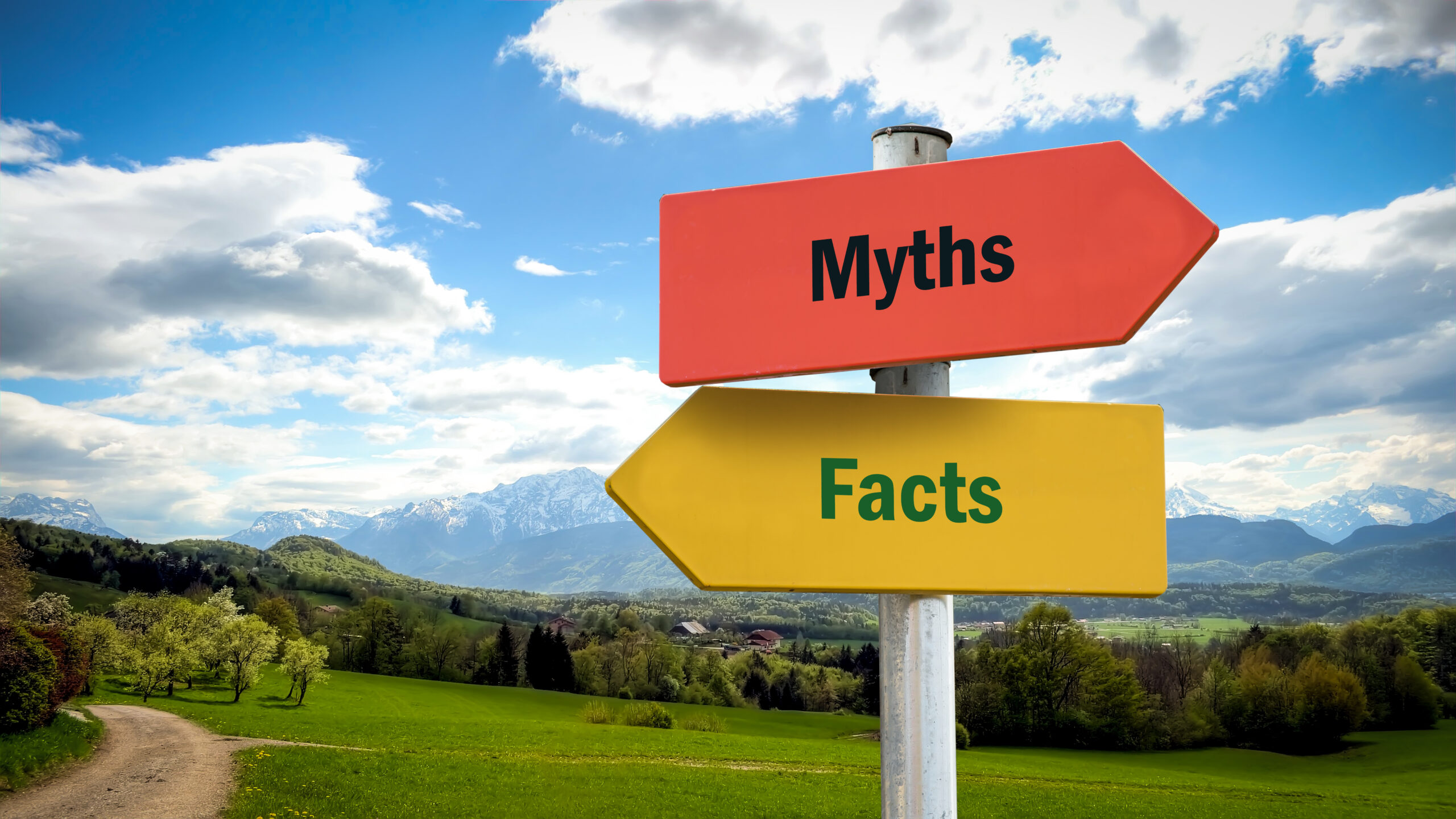 Street Sign to Facts versus Myths with green field, trees, and mountains in the background