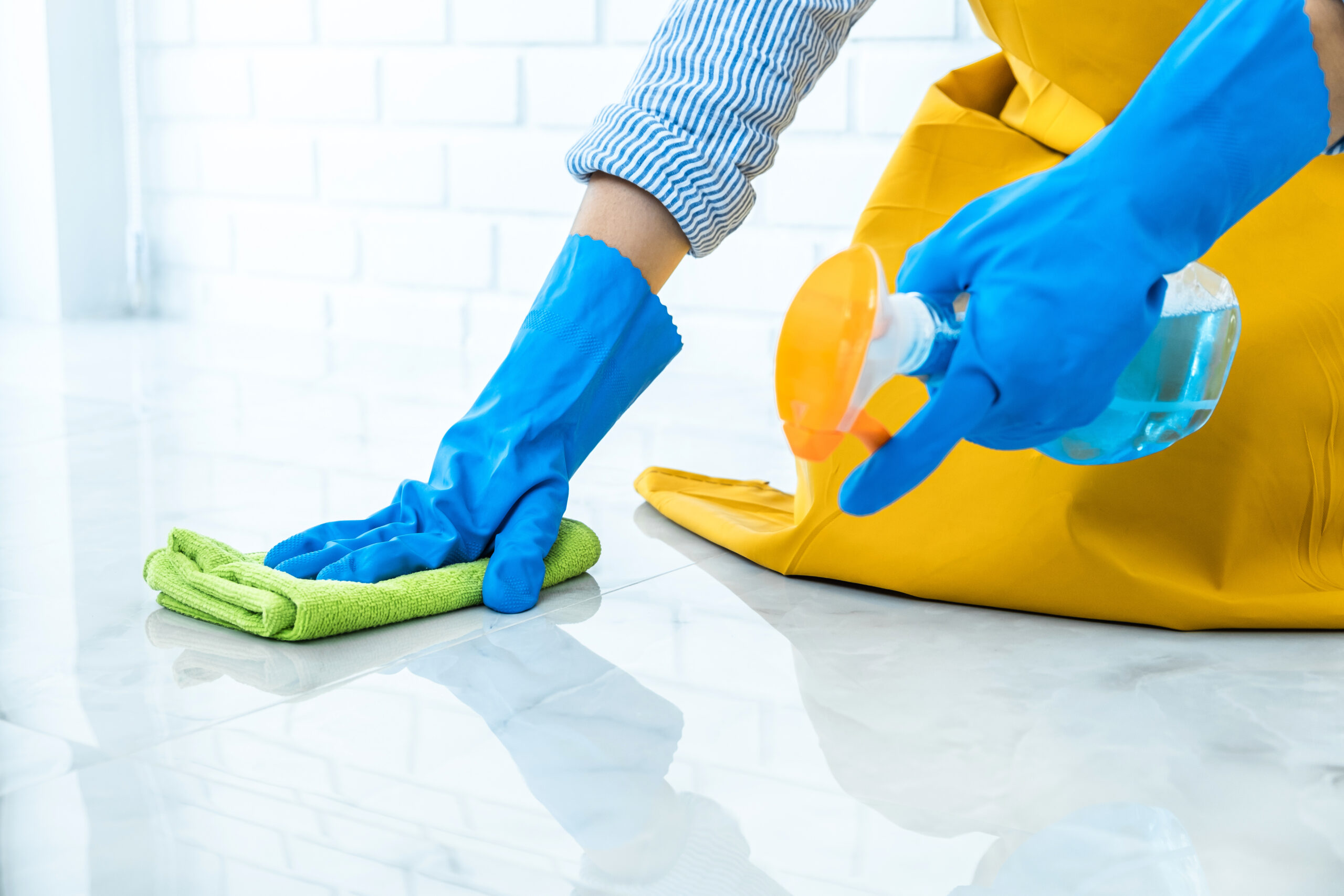 Woman in blue rubber gloves cleaning the floor with a spray bottle and rag to prevent insects