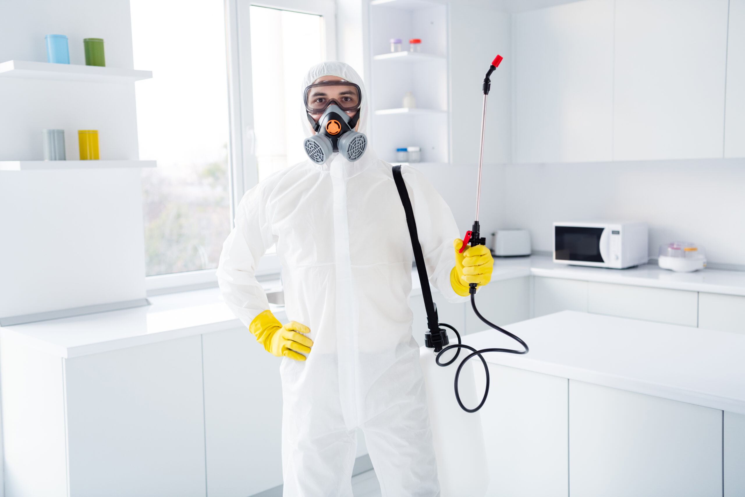 Man in full hazmat suit with sprayer wand ready to apply pesticide to his house
